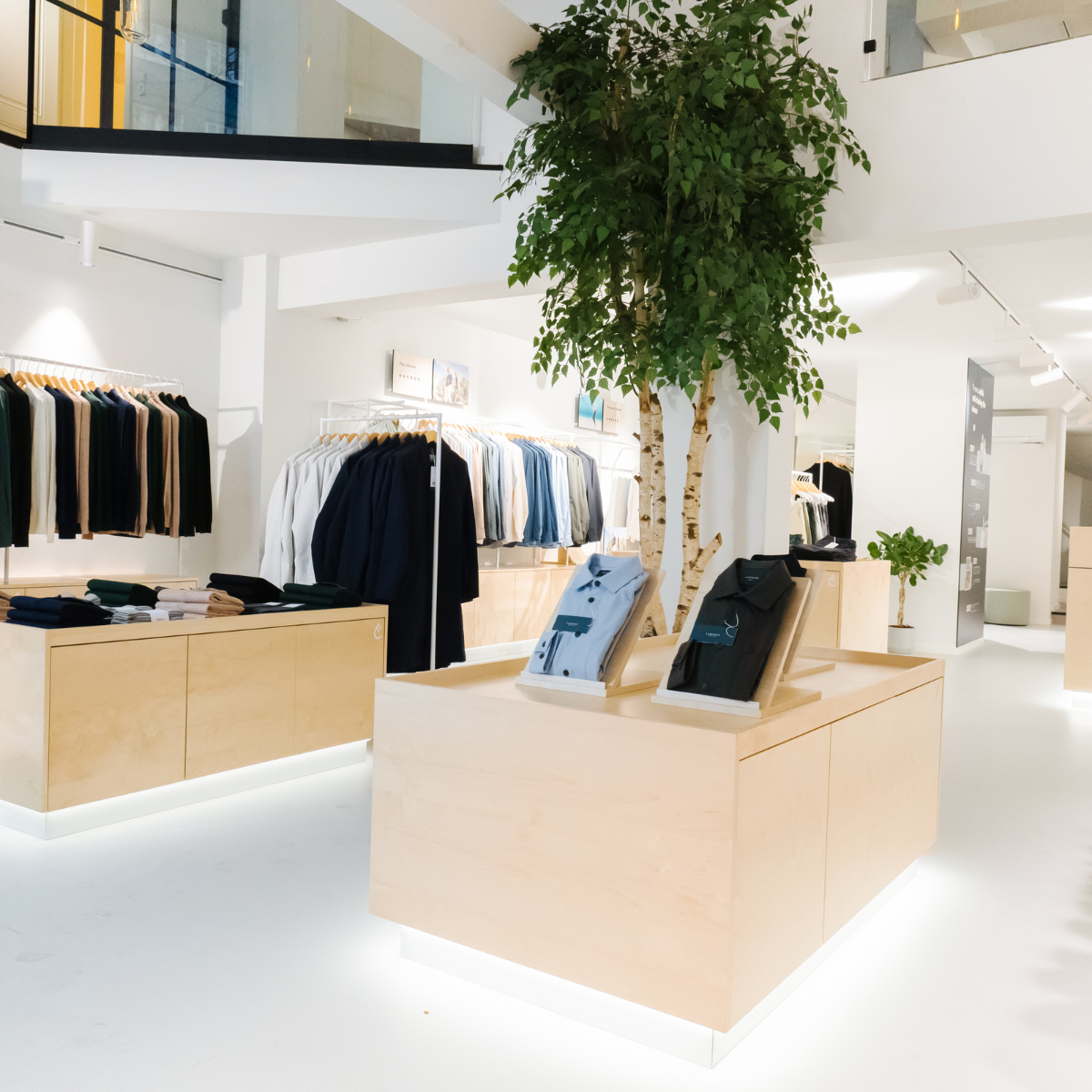 Modern clothing store interior with light wood display counters and hanging clothes.